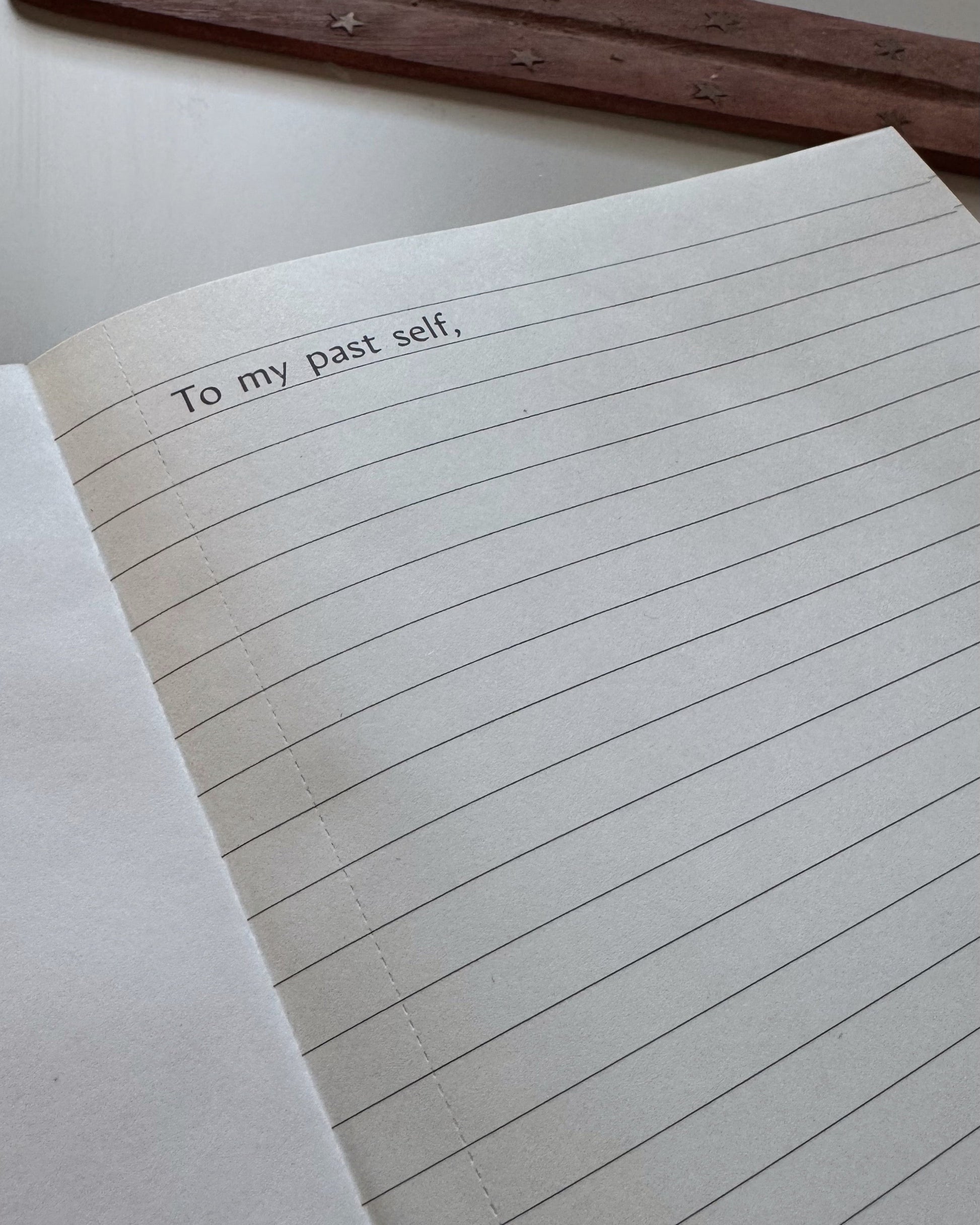 Open notebook with lined pages and text 'To my past self' on a wooden surface.